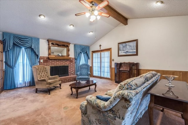 carpeted living room with vaulted ceiling with beams, a wainscoted wall, a fireplace, a textured ceiling, and a ceiling fan