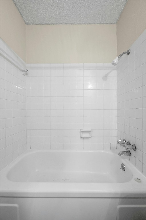 bathroom with a textured ceiling and tiled shower / bath