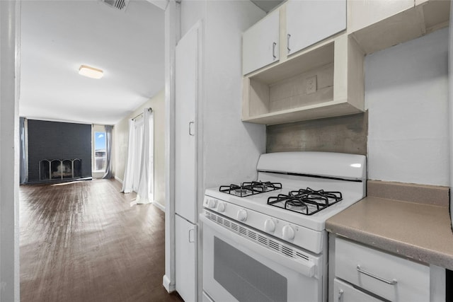 kitchen featuring white cabinetry, dark wood-type flooring, a brick fireplace, and white range with gas stovetop