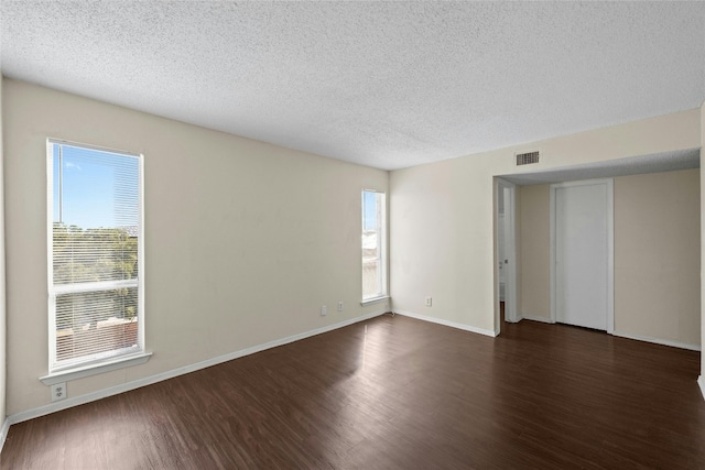 empty room with a wealth of natural light, dark wood-type flooring, and a textured ceiling