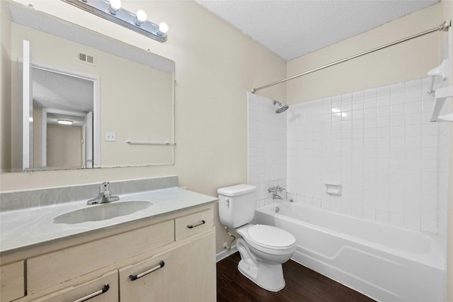 full bathroom featuring toilet, hardwood / wood-style floors, tiled shower / bath combo, vanity, and a textured ceiling