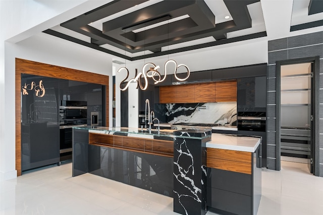 kitchen with sink, a kitchen island with sink, decorative backsplash, and a tray ceiling