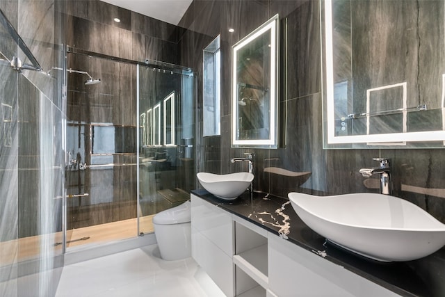 bathroom with vanity, a shower with shower door, toilet, and tile walls