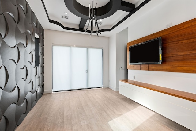 unfurnished living room with an inviting chandelier, light wood-type flooring, and a raised ceiling