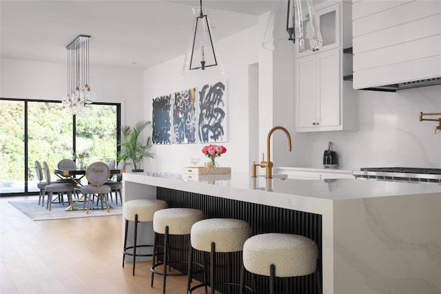 kitchen with white cabinets, sink, hanging light fixtures, light hardwood / wood-style flooring, and a breakfast bar area