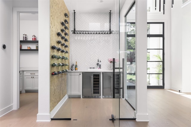 bar featuring white cabinets, stainless steel fridge, light hardwood / wood-style floors, and beverage cooler