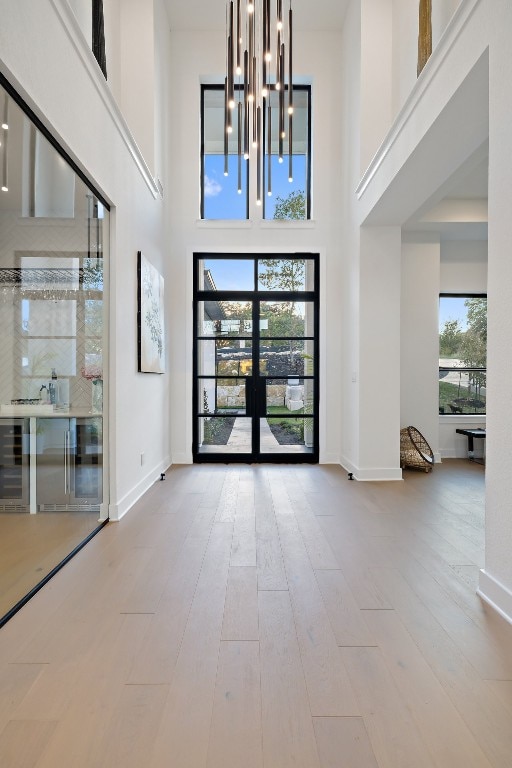 foyer entrance with french doors, light hardwood / wood-style flooring, a healthy amount of sunlight, and a high ceiling