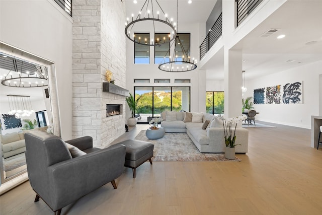 living room featuring a stone fireplace, a chandelier, a high ceiling, and hardwood / wood-style flooring