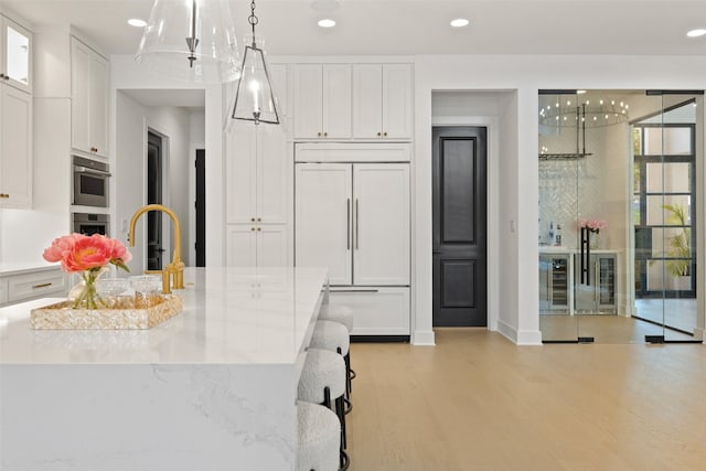 kitchen featuring light wood-type flooring, paneled refrigerator, white cabinetry, and light stone counters