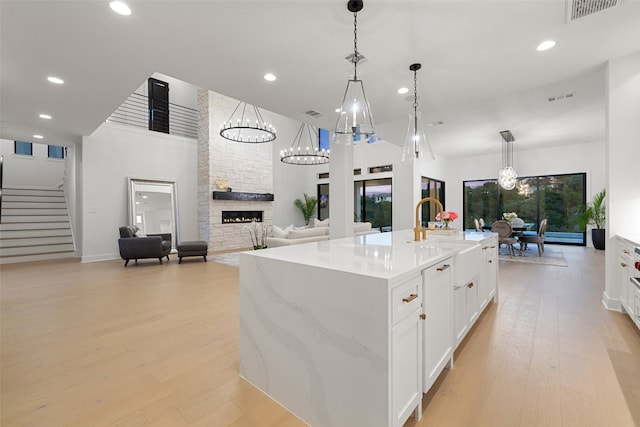 kitchen with pendant lighting, a stone fireplace, an island with sink, and light hardwood / wood-style flooring