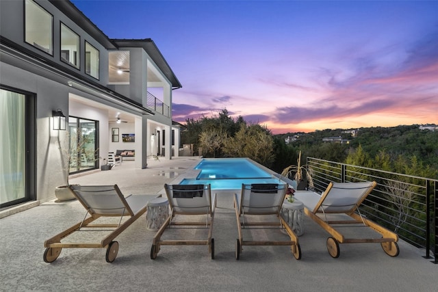 patio terrace at dusk with a balcony, ceiling fan, and a fenced in pool