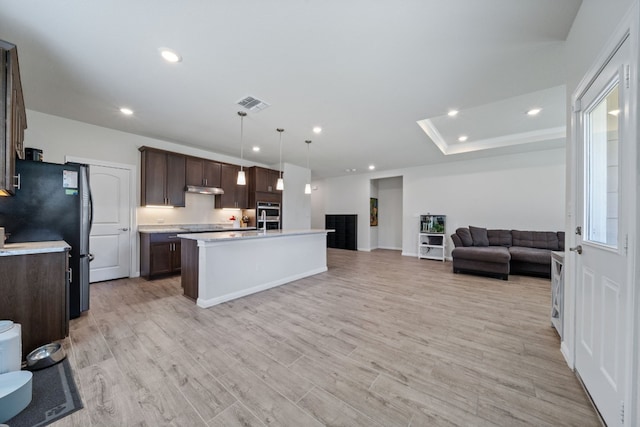 kitchen featuring an island with sink, dark brown cabinets, black fridge, hanging light fixtures, and light hardwood / wood-style flooring