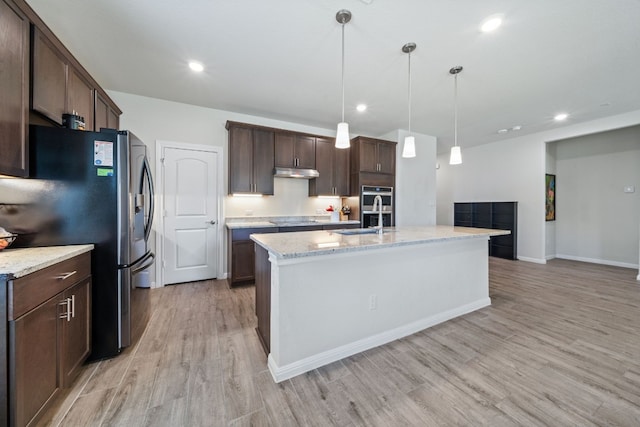 kitchen with hanging light fixtures, appliances with stainless steel finishes, light stone countertops, light wood-type flooring, and dark brown cabinetry