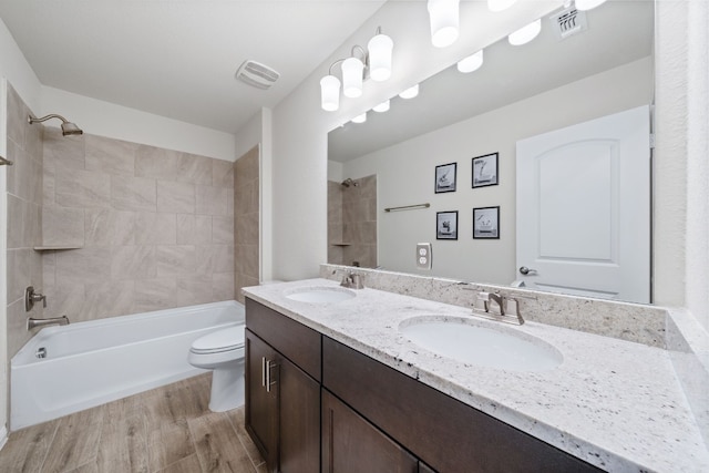 full bathroom with tiled shower / bath, vanity, hardwood / wood-style flooring, and toilet