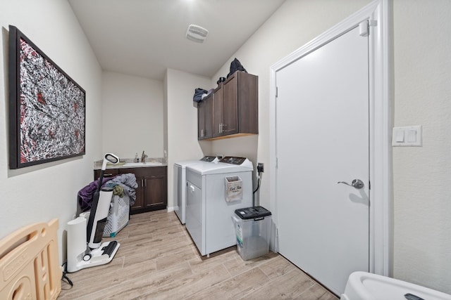 clothes washing area featuring separate washer and dryer, light hardwood / wood-style floors, and cabinets