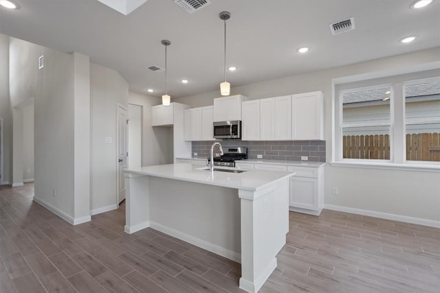 kitchen featuring stainless steel appliances, a kitchen island with sink, sink, decorative light fixtures, and white cabinets