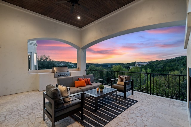 patio terrace at dusk featuring exterior kitchen, an outdoor hangout area, ceiling fan, area for grilling, and a balcony