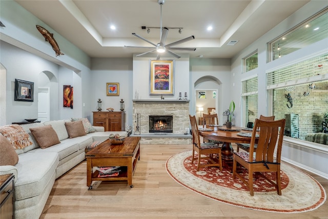 living room with a fireplace, a tray ceiling, light wood-type flooring, and ceiling fan