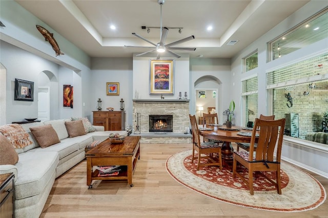 7618 Turnback Ledge Trl, Lago Vista, TX 78645 - living room with arched walkways, a tray ceiling, a fireplace, a ceiling fan, and light wood finished floors