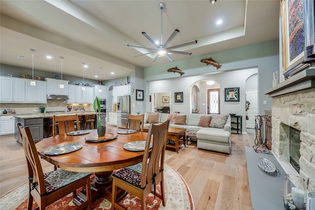 dining area with light hardwood / wood-style flooring, a stone fireplace, and ceiling fan