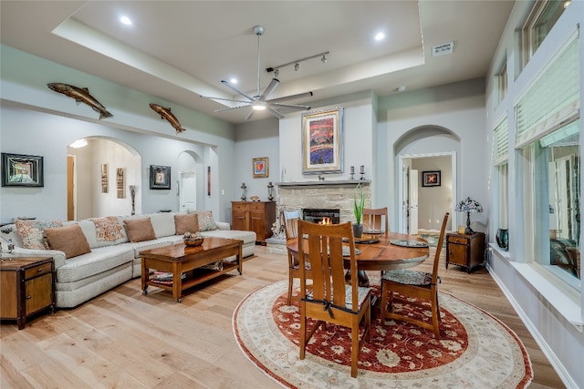 dining space with track lighting, ceiling fan, a tray ceiling, light wood-type flooring, and a fireplace