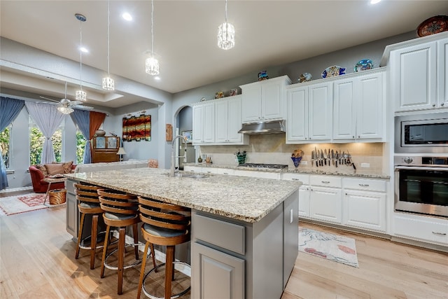 kitchen with appliances with stainless steel finishes, hanging light fixtures, a kitchen island with sink, and white cabinetry