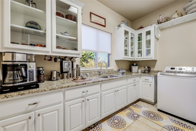 kitchen with washer / clothes dryer, sink, light tile patterned floors, white cabinetry, and light stone counters