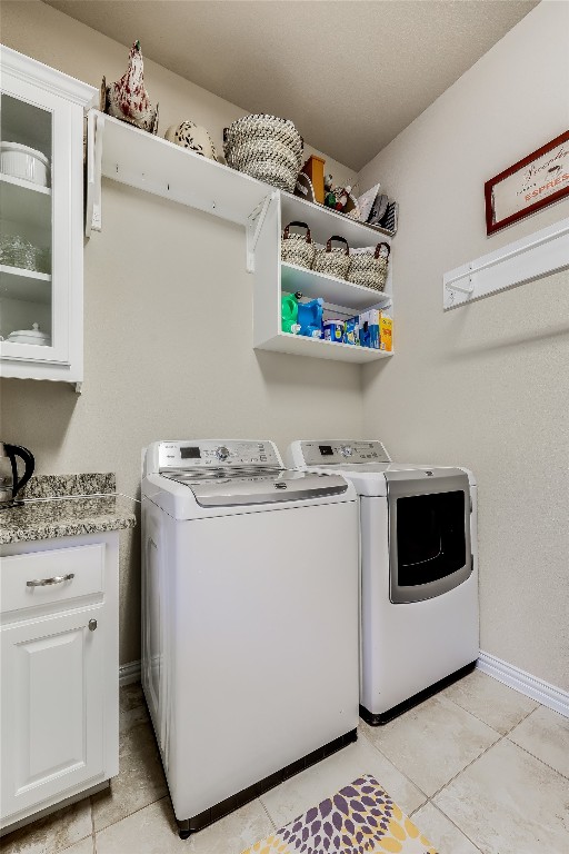 washroom with washing machine and dryer, light tile patterned floors, and cabinets