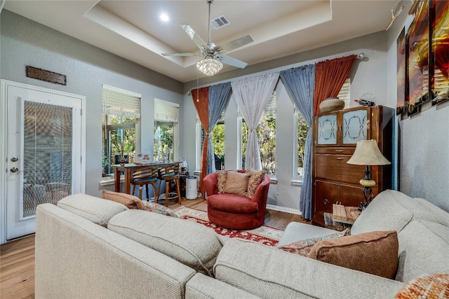 living room with plenty of natural light, light hardwood / wood-style flooring, a raised ceiling, and ceiling fan