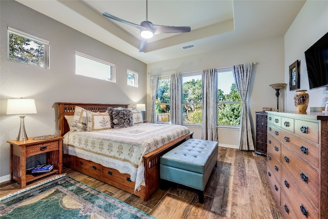 bedroom with dark hardwood / wood-style floors, a tray ceiling, and ceiling fan