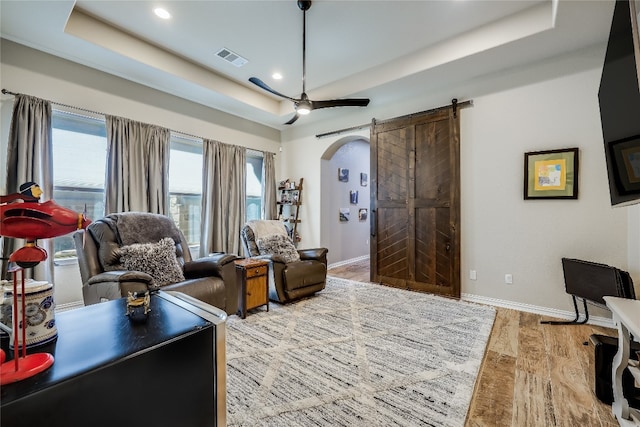 living room with a barn door, plenty of natural light, and a raised ceiling