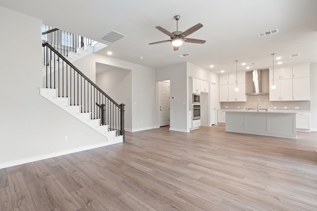 unfurnished living room with sink, light wood-type flooring, and ceiling fan