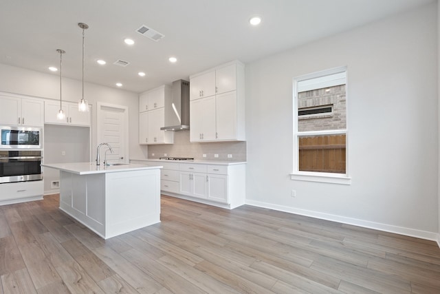 kitchen with wall chimney exhaust hood, white cabinetry, a kitchen island with sink, and stainless steel appliances