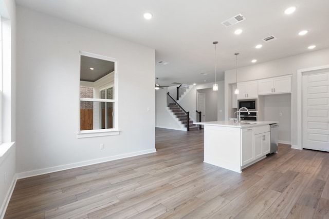 kitchen with a kitchen island with sink, light hardwood / wood-style flooring, decorative light fixtures, and white cabinetry