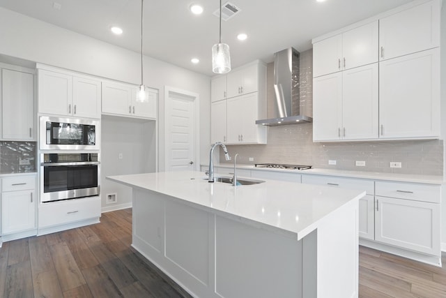 kitchen with wall chimney exhaust hood, wood-type flooring, sink, white cabinetry, and appliances with stainless steel finishes