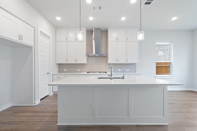 kitchen with a center island with sink, sink, white cabinetry, and wall chimney range hood