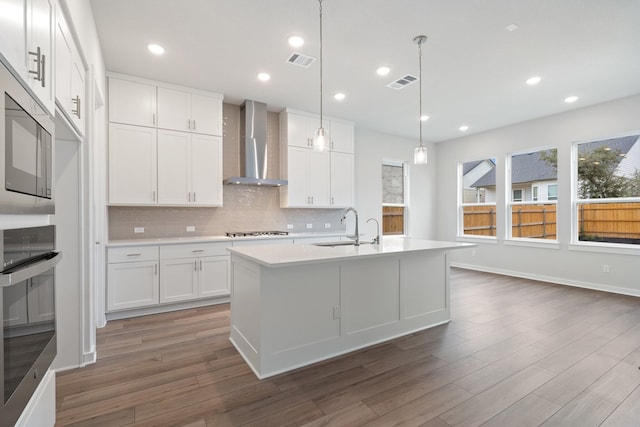 kitchen featuring wall chimney range hood, white cabinets, stainless steel appliances, and pendant lighting