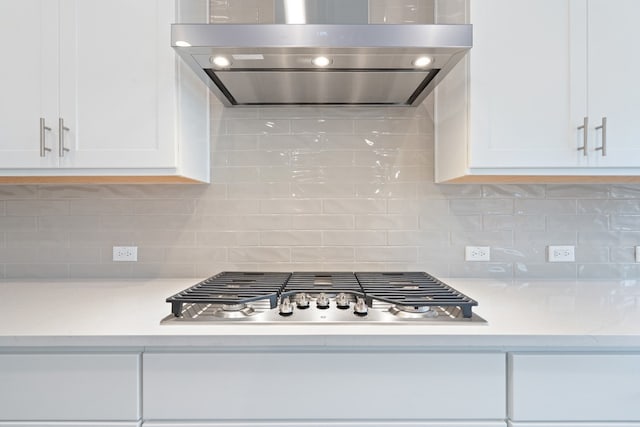 kitchen with tasteful backsplash, white cabinets, stainless steel gas stovetop, light stone counters, and ventilation hood