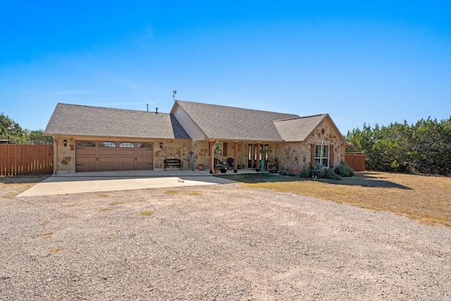 view of front of property with stone siding, driveway, an attached garage, and fence