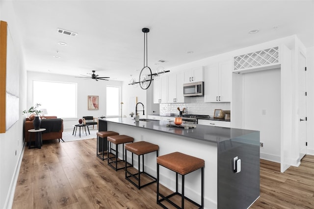 kitchen with appliances with stainless steel finishes, sink, an island with sink, dark hardwood / wood-style flooring, and white cabinetry