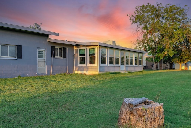 back house at dusk with a yard and a sunroom