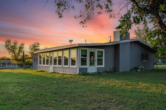 back house at dusk featuring central air condition unit and a lawn