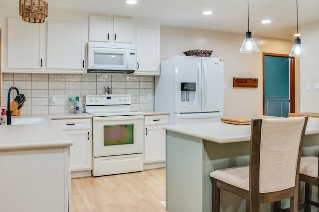 kitchen with white appliances, sink, white cabinetry, light hardwood / wood-style floors, and a breakfast bar area