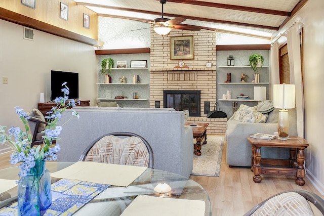 living room with lofted ceiling with beams, a brick fireplace, light hardwood / wood-style floors, and ceiling fan