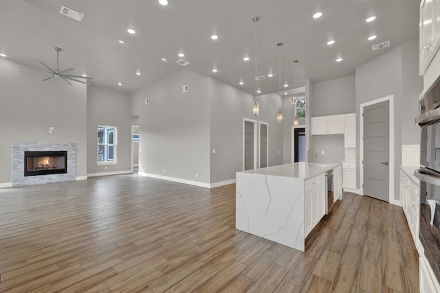 kitchen featuring a towering ceiling, white cabinets, and a center island with sink