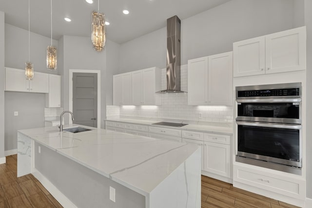 kitchen with wall chimney range hood, sink, stainless steel double oven, decorative light fixtures, and white cabinets