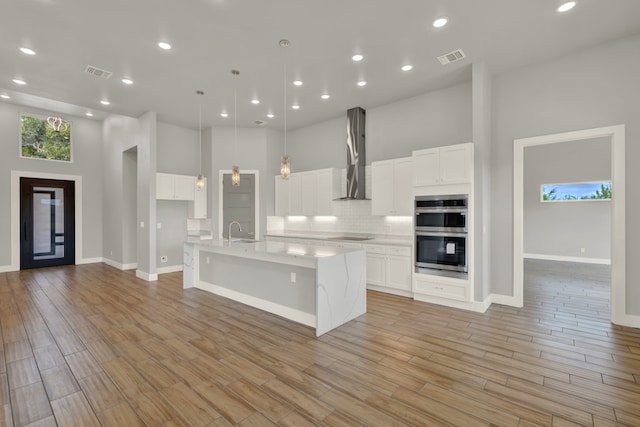 kitchen with white cabinetry, wall chimney exhaust hood, a high ceiling, and stainless steel double oven