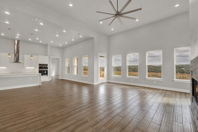 unfurnished living room with a towering ceiling, dark hardwood / wood-style floors, and ceiling fan