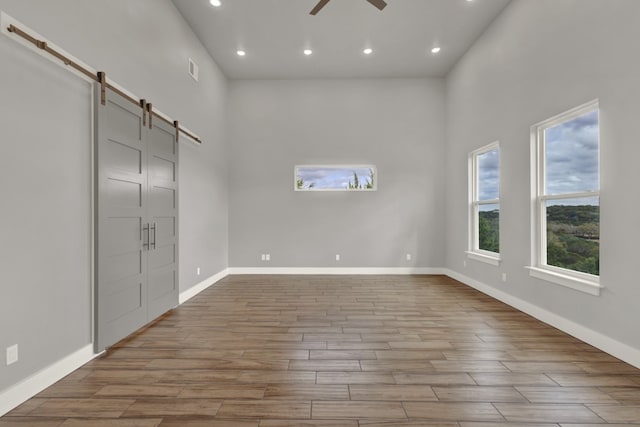 spare room with a high ceiling, a barn door, light hardwood / wood-style flooring, and ceiling fan