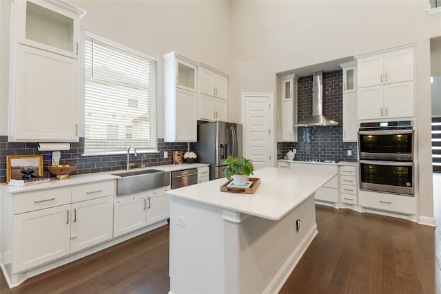 kitchen featuring white cabinets, a kitchen island, appliances with stainless steel finishes, dark hardwood / wood-style floors, and wall chimney exhaust hood